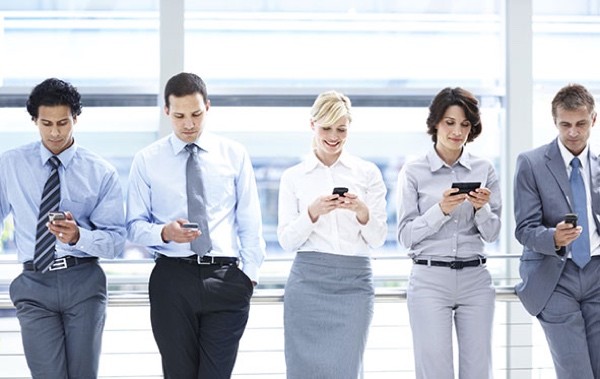 A group of executives standing in line and looking at their smartphones